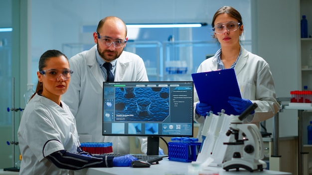 Team di scienziati seduti in laboratorio che guarda l'obbiettivo nel moderno laboratorio attrezzato. Gruppo di medici che esaminano l'evoluzione del virus utilizzando l'alta tecnologia per la ricerca scientifica, lo sviluppo di vaccini.