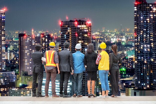 Team di uomini d'affari internazionali con ingegneri professionisti in piedi sulla torre di luce del grattacielo in background urbano