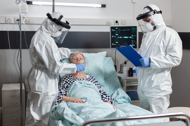 Team medico in clinica che indossa tuta dpi e visiera durante la visita del paziente nella stanza d'ospedale in tempo di coronavirus per prevenire l'infezione