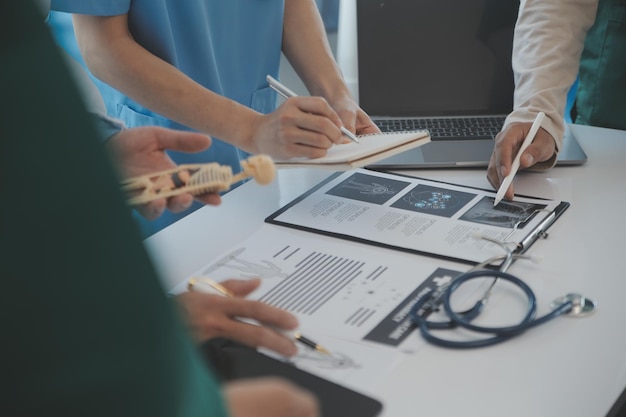 Team medico multirazziale che ha un incontro con medici in camici bianchi e scrub chirurgici seduti a un tavolo che discutono dei record di un paziente