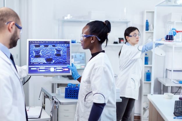 Team multietnico di ricercatori medici che lavorano insieme in un laboratorio sterile indossando occhiali e guanti protettivi.