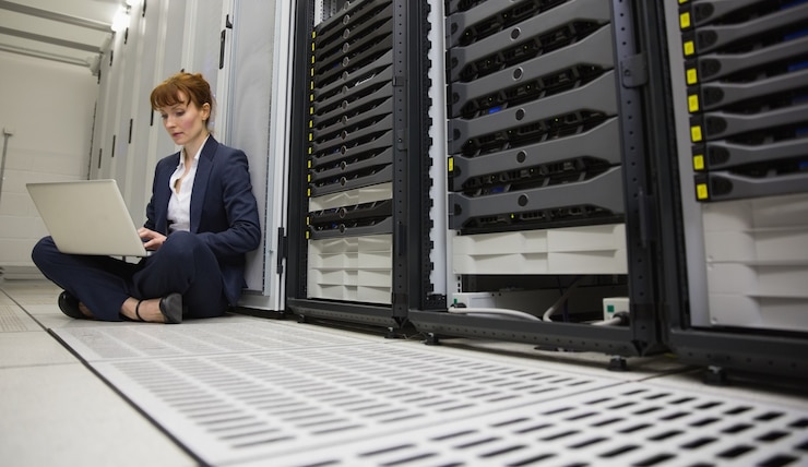 Photo technician sitting on floor beside server tower using laptop