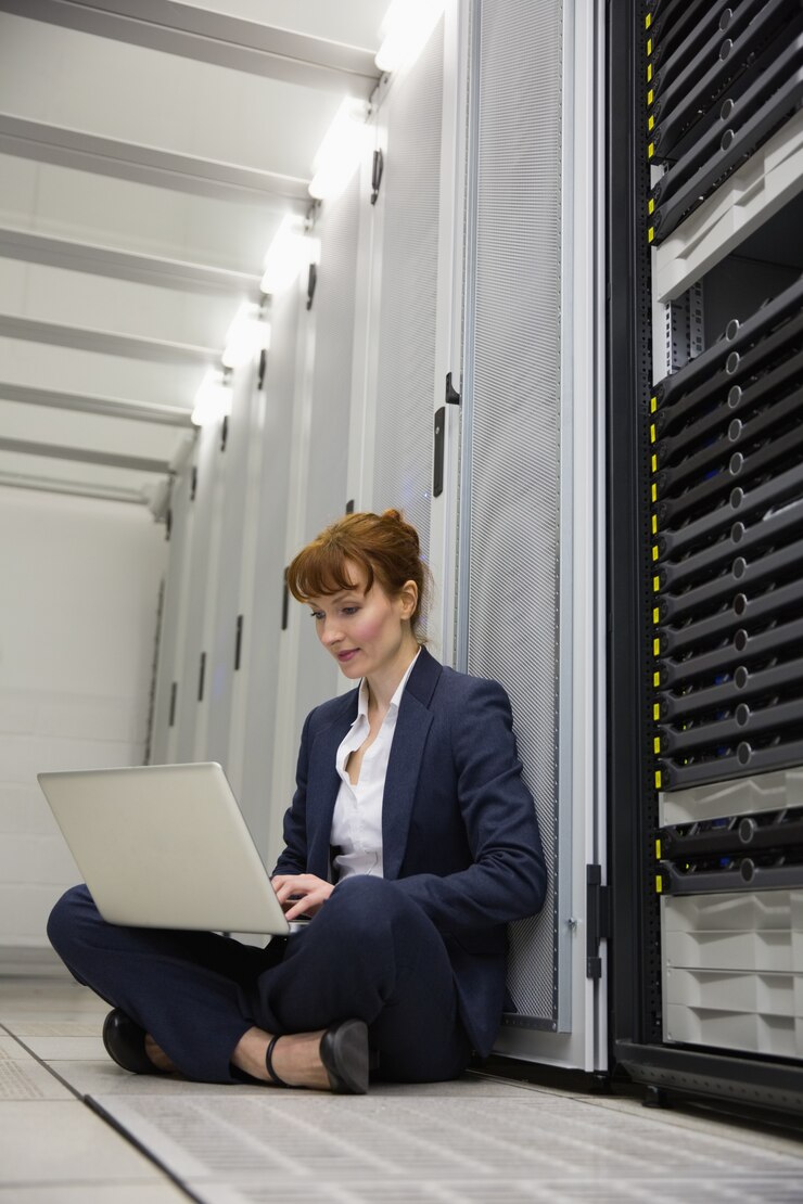 Photo technician sitting on floor beside server tower using laptop