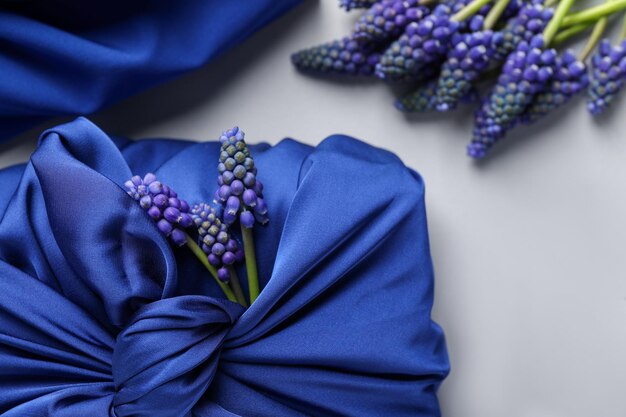 Tecnica Furoshiki Regalo confezionato in tessuto di seta blu fiori di muscari e nastro su tavolo bianco close-up