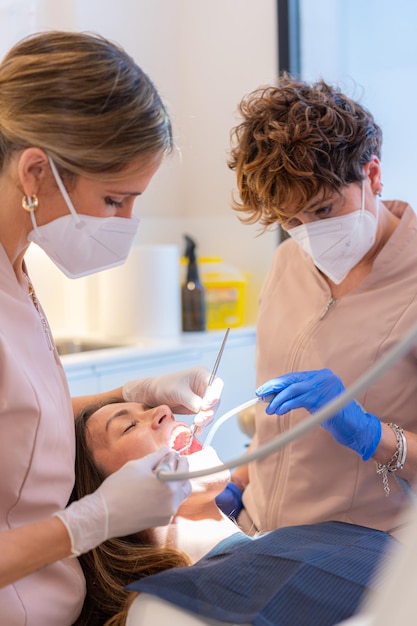 Tecnico che esamina la bocca di una donna sdraiata su una sedia in una clinica dentistica