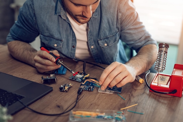 Tecnico concentrato sulla riparazione di apparecchiature elettroniche mediante saldatore.