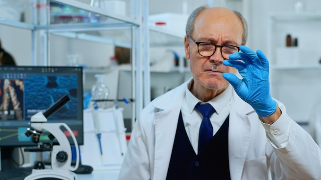 Tecnico di laboratorio uomo maturo guardando il campione di virus in un moderno laboratorio attrezzato. Scienziato che lavora con vari tessuti batterici e analisi del sangue, concetto di ricerca farmaceutica per antibiotici