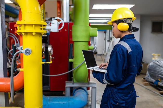 Tecnico di manutenzione presso un impianto di riscaldamento I lavoratori petrolchimici supervisionano il funzionamento dei gasdotti e degli oleodotti nella fabbrica Gli ingegneri mettono la protezione dell'udito In una stanza con molti tubi