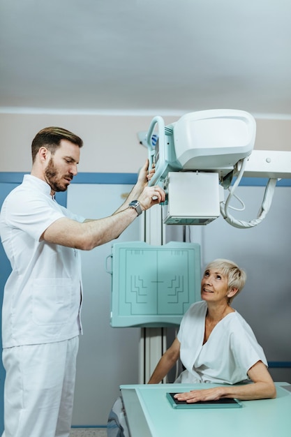 Tecnico medico e paziente di sesso femminile maturo durante la procedura a raggi X della mano in clinica
