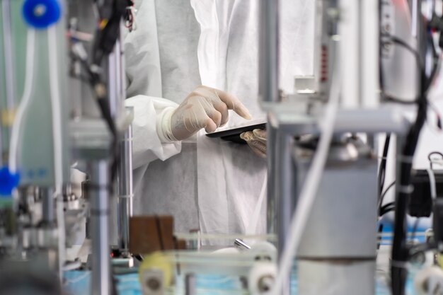 Tecnico professionista in panni sterili e macchina per il controllo e la lavorazione della maschera facciale nella fabbrica di maschere chirurgiche. fabbrica di industria e concetto di persone. al chiuso