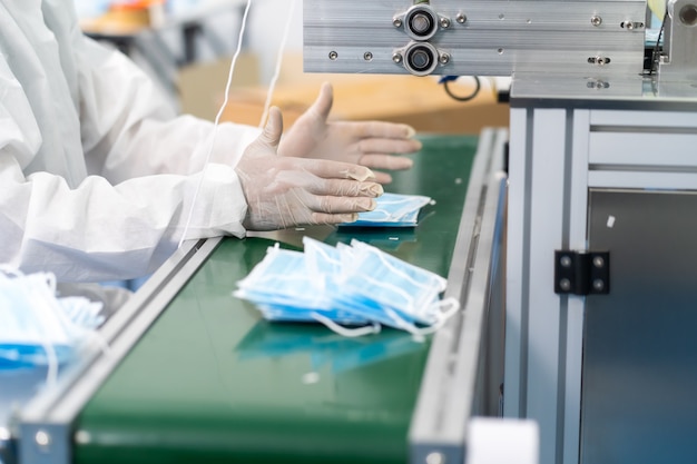 Tecnico professionista in panni sterili e macchina per il controllo e la lavorazione della maschera facciale nella fabbrica di maschere chirurgiche. fabbrica di industria e concetto di persone. al chiuso