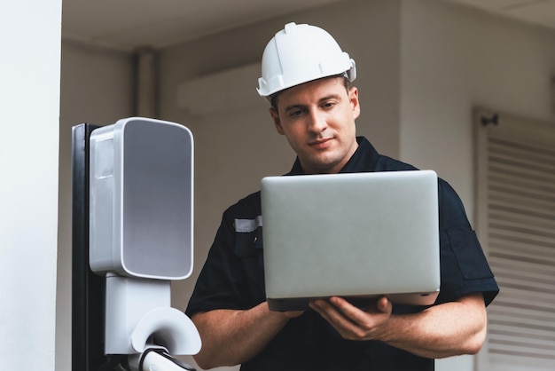 Tecnico qualificato che lavora all'installazione di stazioni di ricarica di veicoli elettrici a domicilio che esegue la risoluzione dei problemi e la configurazione del sistema di ricarica con laptop per veicoli elettrici a domicilio Synchronos