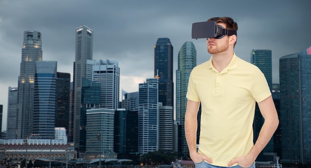 Tecnologia 3d, realtà virtuale, viaggi, intrattenimento e concetto di persone - giovane uomo con cuffie per realtà virtuale o occhiali 3d su sfondo di grattacieli della città di singapore
