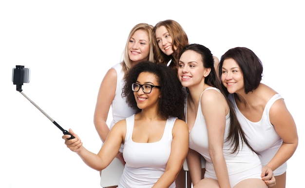 tecnologia, amicizia, corpo positivo e concetto di persone - gruppo di donne felici in biancheria intima bianca che scattano foto con lo smartphone sul selfie stick