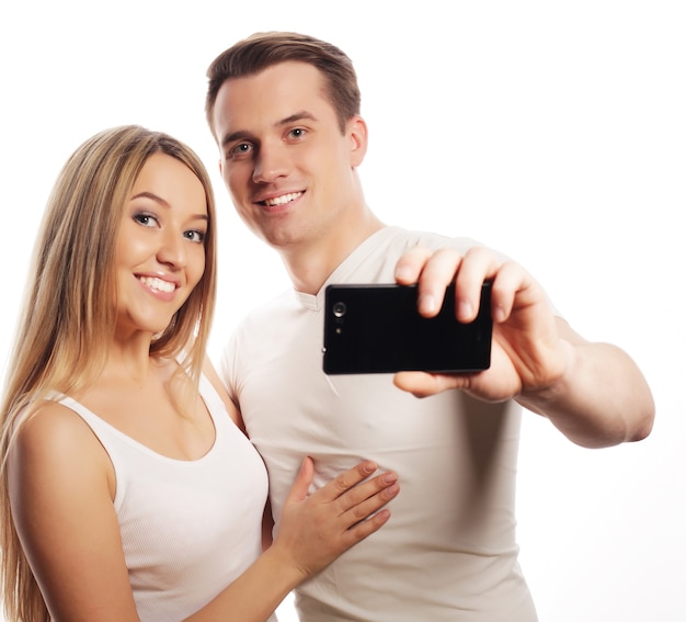 Tecnologia, amore e concetto di amicizia - coppia sorridente con smartphone, selfie e divertimento. Studio girato su sfondo bianco.