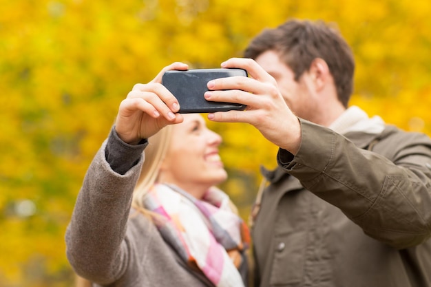 tecnologia, amore, relazione e concetto di persone - primo piano di una coppia sorridente che si fa selfie con lo smartphone nel parco autunnale