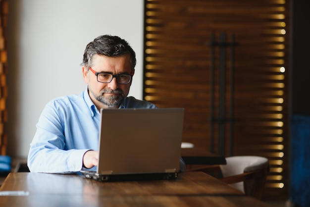 Tecnologia aziendale e concetto di persone Uomo d'affari senior con computer portatile che beve caffè al caffè moderno