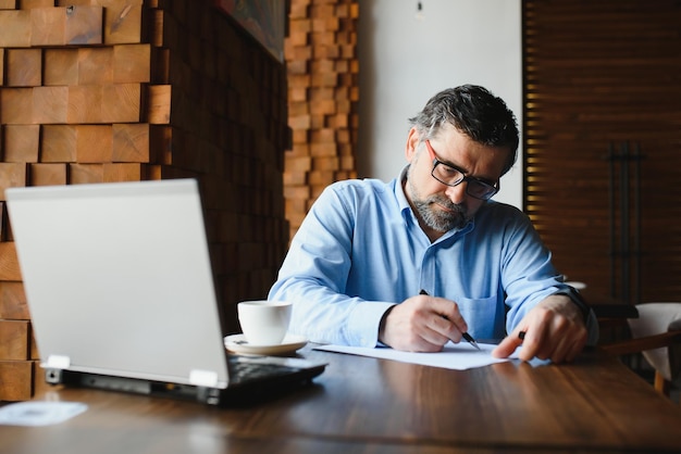 Tecnologia aziendale e concetto di persone Uomo d'affari senior con computer portatile che beve caffè al caffè moderno