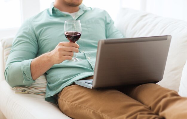 tecnologia, bevande, tempo libero, casa e concetto di stile di vita - primo piano dell'uomo primo piano dell'uomo con laptop e bicchiere di vino a casa