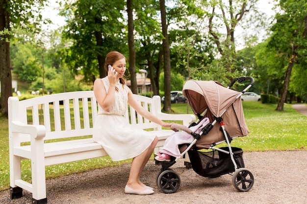 tecnologia della maternità e concetto di persone madre felice con la bambina in passeggino che chiama sullo smartphone al parco estivo