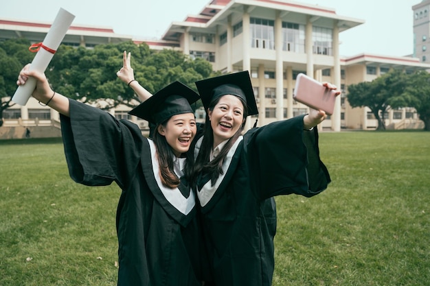 tecnologia di laurea dell'istruzione e concetto di persone. gruppo di studenti internazionali felici in tavole di mortaio e abiti da scapolo con diplomi che si fanno selfie con lo smartphone all'aperto in una giornata di sole estivo.