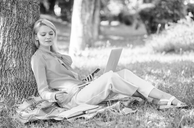 Tecnologia educativa e concetto di Internet Donna con un computer portatile che lavora all'aperto magra sul tronco d'albero Ragazza che lavora con un computer portatile nel parco seduto sull'erba Ambiente naturale Ufficio Lavora all'aperto benefici