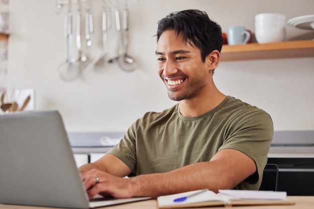 Tecnologia Internet e cucina uomo con laptop felice lavoratore freelance dall'India Avvio lavoro da casa Uomo d'affari indiano con sorriso facendo ricerche online e digitando sul computer con notebook