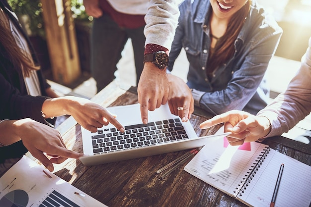 Tecnologia per aumentare la produttività Scatto ritagliato di un team di colleghi che usano un laptop insieme durante una riunione in un bar all'aperto