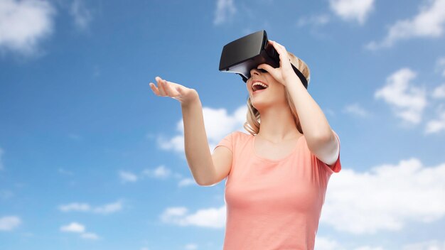 tecnologia, realtà virtuale, intrattenimento e concetto di persone - giovane donna felice con cuffie per realtà virtuale o occhiali 3d su sfondo blu cielo e nuvole