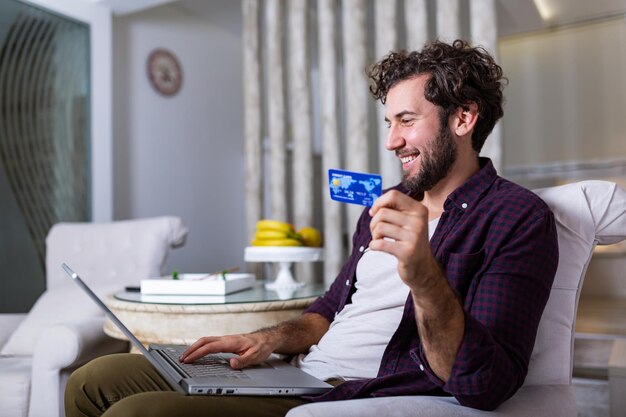 Tecnologia, shopping, banche, casa e concetto di stile di vita - primo piano dell'uomo con computer portatile e carta di credito a casa. Giovane che utilizza la carta di credito per lo shopping online.