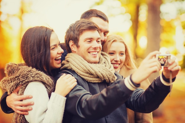 tecnologia, vacanze, viaggi, concetto di persone felici - gruppo di amici o coppie che si divertono con la macchina fotografica nel parco autunnale