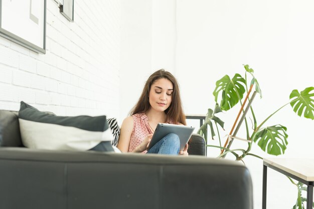 Tecnologie, comunicazione, concetto di persone: la giovane donna è seduta sul divano in pelle e sta utilizzando