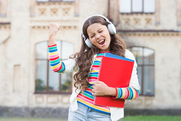 Tecnologie digitali per l'apprendimento Studentessa porta quaderni e cuffie Tecnologie per lo studio Audio corso Tecnologie moderne Elearning e metodi moderni Ascolto libro di scuola