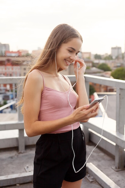 Tecnologie, emozioni, persone, musica, bellezza, moda e concetto di stile di vita - Giovane donna con le cuffie che penzolano sul suo telefono cellulare mentre cammina in una strada urbana, vista dall'alto