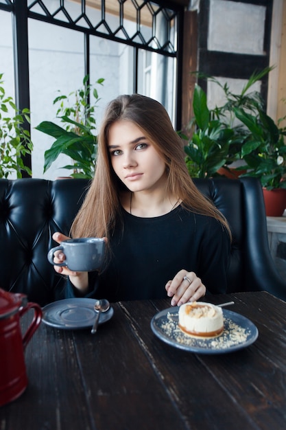 Tecnologie, emozioni, stile di vita, persone, concetto di adolescenti - Giovane donna felice che legge sul suo telefono cellulare mentre è seduta in un moderno interno della caffetteria, splendida ragazza hipster con un bel sorriso