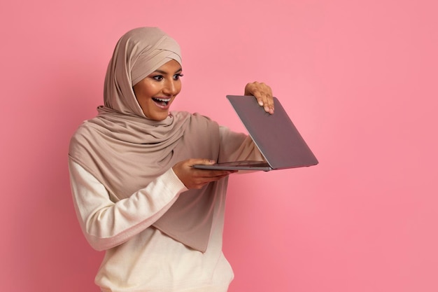 Tecnologie moderne felice donna musulmana in hijab che apre il computer portatile con eccitazione