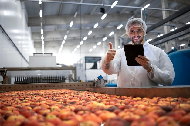 Tecnologo che mostra i pollici in su nella fabbrica di trasformazione alimentare e controlla la qualità della frutta della mela.