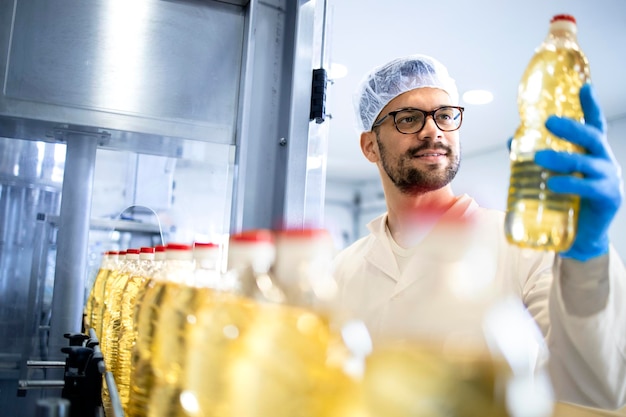 tecnologo lavoratore che tiene una bottiglia di olio vegetale per il controllo e la qualità nell'impianto di produzione alimentare