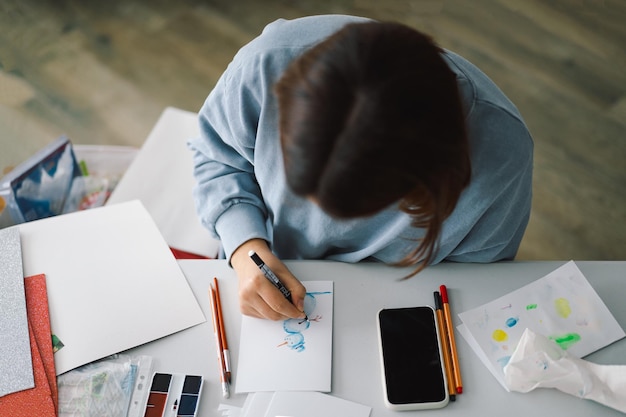 Teengirl ragazza fa un'applicazione di carta di carta colorata con il pupazzo di neve Il concetto di creatività La ragazza fa artigianato carta da cartolina carta multicolore per la creatività Lavorare da casa Hobby