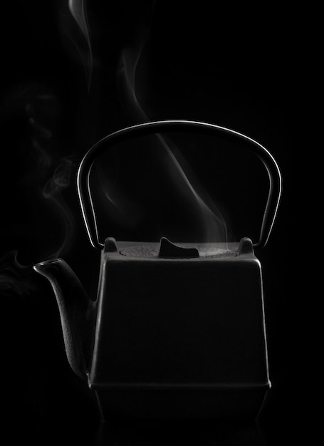 Teiera asiatica in ferro nero con vapore su sfondo nero