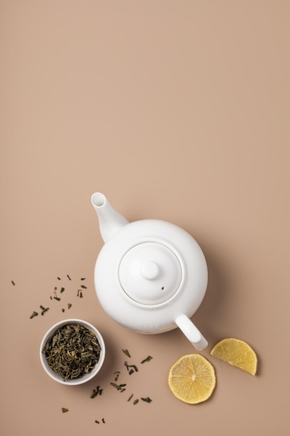 Teiera bianca con tè verde sfuso in tazza e limone su fondo beige