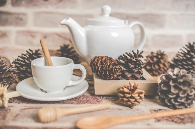 Teiera bianca di concetto del tè con la tazza di tè bianca con le foglie secche su fondo di legno