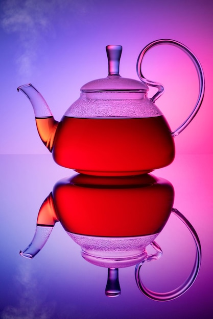Teiera con tè caldo su sfondo colorato. Bollitore in vetro con vapore