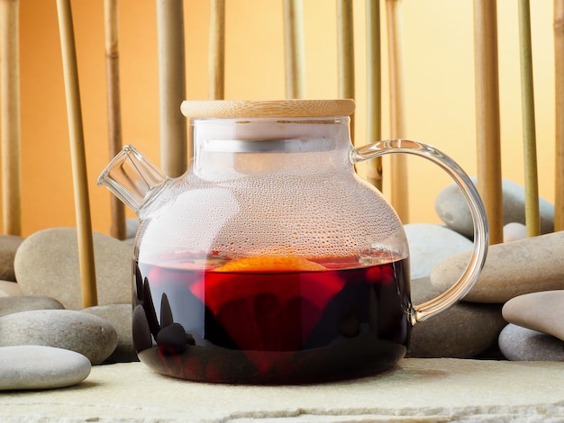 Teiera di vetro con karkade caldo del tè della bacca rossa, primo piano. Tè sullo sfondo di un boschetto di bambù e pietre. Concetto di tea party cinese tradizionale. Giornata internazionale del tè, sfondo.