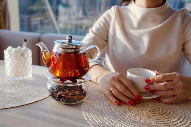 Teiera di vetro con tè al caffè. Mani della donna con la tazza di tè su fondo