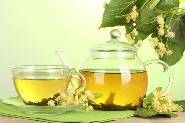 Teiera e tazza con tè di tiglio e fiori sulla tavola di legno su sfondo verde