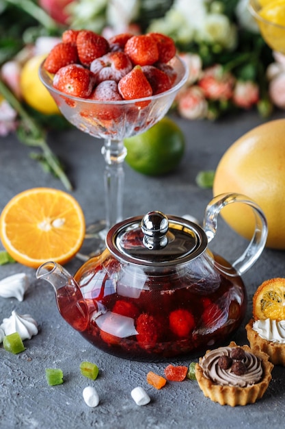 Teiera in vetro con tè al lampone e menta su sfondo blu con frutta e decorazioni