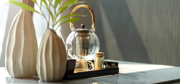 Teiera in vetro su vassoio da tè in legno con vaso di fiori bianchi su tavolo da pranzo in marmo con parasole nel concetto di sfondo della casa del soggiorno