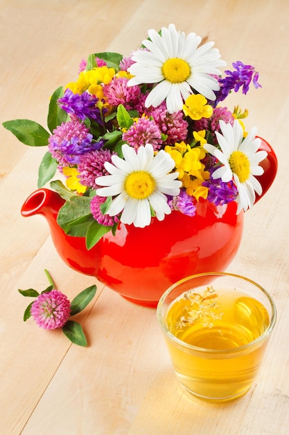Teiera rossa con bouquet di erbe curative e fiori tazza di tè sano sul tavolo erboristeria
