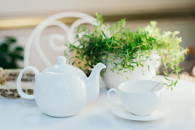 Teiere in ceramica bianche e ingredienti per il tè, in cima a un tavolo bianco con un vaso di fiori.